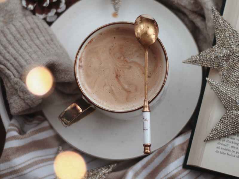 Cup of hot chocolate with gold spoon, silver ornamental stars and gold and white background