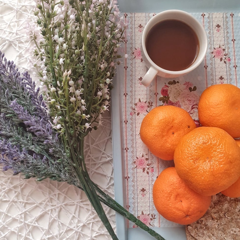 fresh fruit oranges beside porcelain mug with purple and whitedried flowers